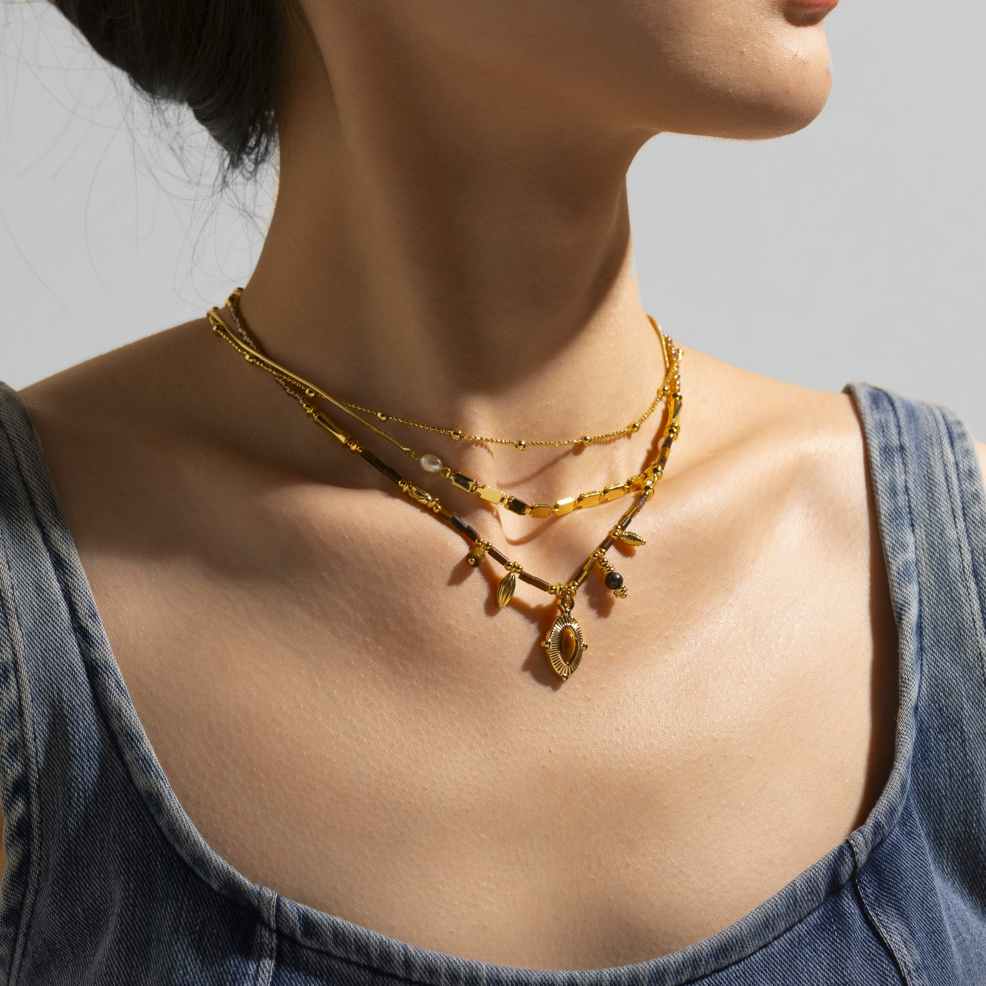 FY’s oval tiger eye necklace with 18K gold-plated chain, styled with black sweater for minimalist elegance.
